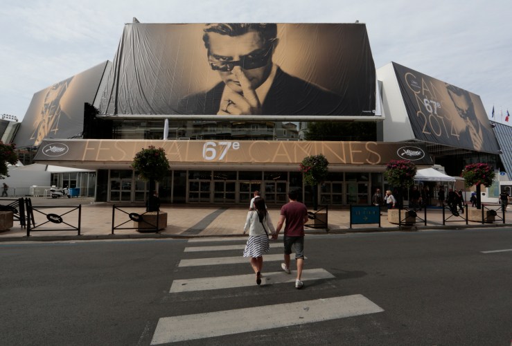 People walk past the Festival Palace displaying a giant canvas of the official poster of the 67th Cannes Film Festival featuring actor Marcello Mastroianni in Cannes